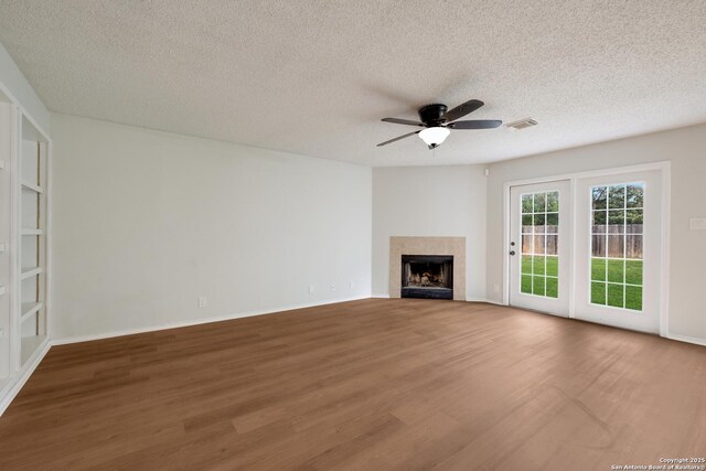 unfurnished living room featuring wood finished floors, a textured ceiling, ceiling fan, a fireplace, and baseboards