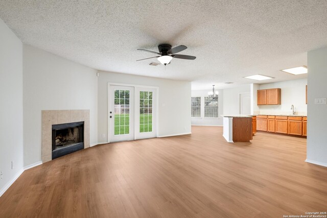 unfurnished living room with a sink, light wood-type flooring, a fireplace, a textured ceiling, and ceiling fan with notable chandelier