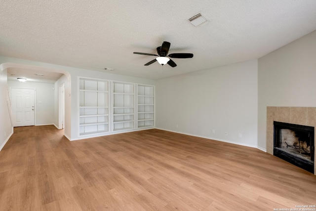 unfurnished living room with visible vents, a ceiling fan, arched walkways, light wood-style floors, and a textured ceiling