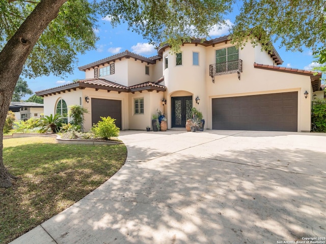 mediterranean / spanish-style house with a garage, concrete driveway, a tiled roof, and stucco siding