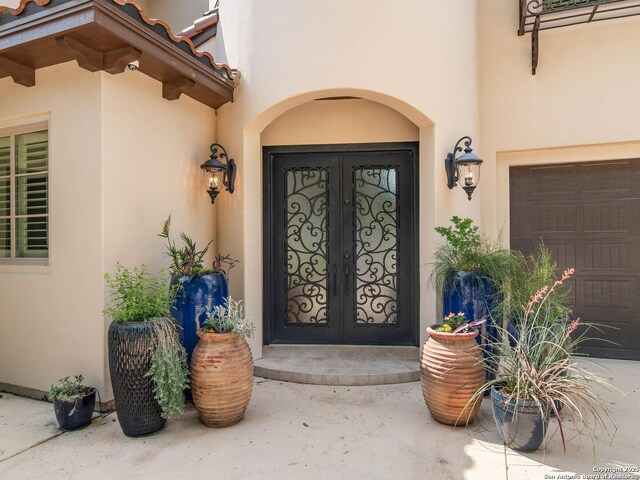 view of exterior entry with stucco siding, a garage, and french doors