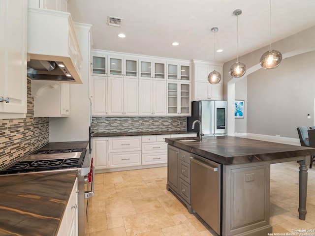 kitchen featuring stainless steel appliances, a sink, visible vents, custom exhaust hood, and wooden counters