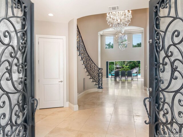 foyer entrance with visible vents, light tile patterned flooring, arched walkways, stairs, and a notable chandelier