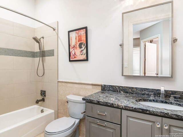 bathroom featuring washtub / shower combination, a wainscoted wall, toilet, vanity, and tile walls