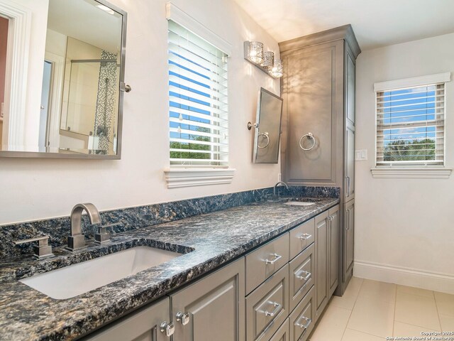 bathroom featuring baseboards, tile patterned flooring, a sink, and double vanity