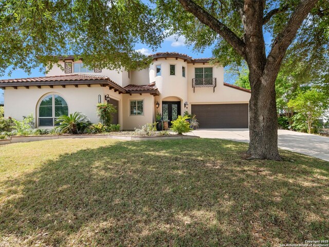 mediterranean / spanish house with a tile roof, a front lawn, driveway, and stucco siding