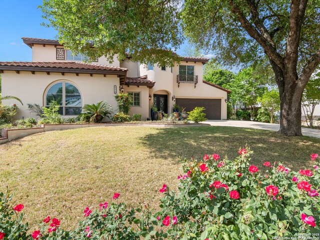 mediterranean / spanish house featuring a tiled roof, driveway, a front yard, and stucco siding