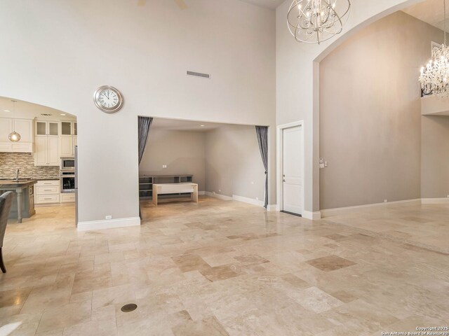 entryway featuring arched walkways, visible vents, baseboards, a towering ceiling, and an inviting chandelier