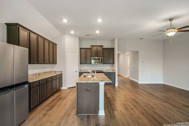 kitchen with a ceiling fan, dark brown cabinets, baseboards, appliances with stainless steel finishes, and light stone countertops