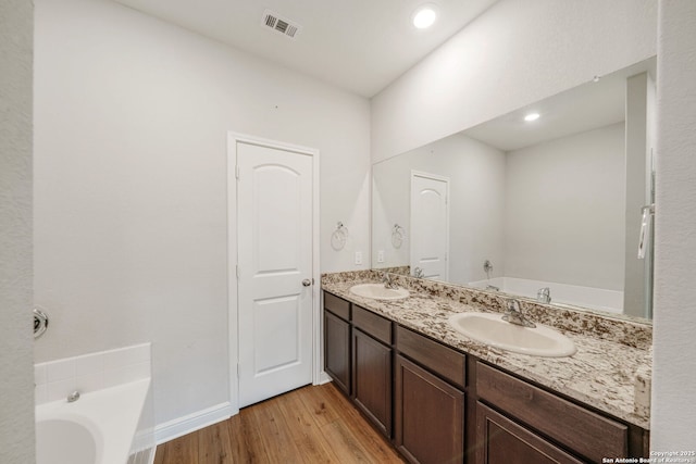 bathroom with a bath, wood finished floors, a sink, and visible vents