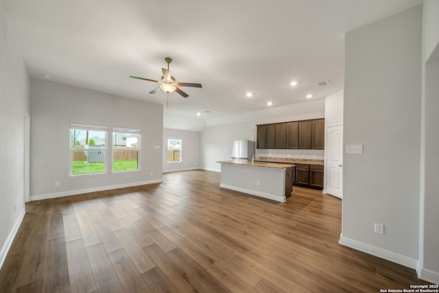 kitchen with an island with sink, open floor plan, ceiling fan, dark wood-type flooring, and freestanding refrigerator