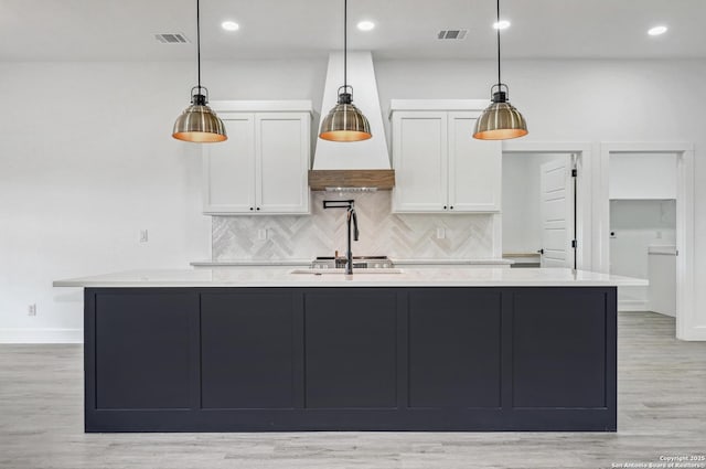 kitchen with white cabinets, light wood finished floors, visible vents, decorative backsplash, and an island with sink