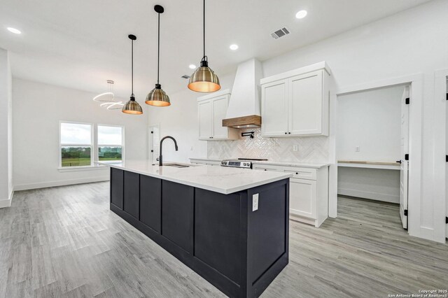 kitchen featuring white cabinets, a sink, visible vents, backsplash, and premium range hood