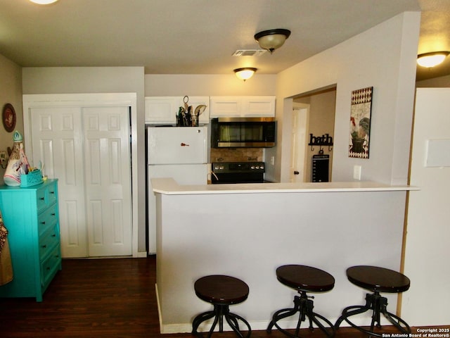 12365 Rudolph Rd, Atascosa, TX 78002 - kitchen with stainless steel microwave, dark wood-style flooring, a kitchen bar, white cabinetry, and black range with electric stovetop