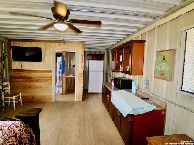 12365 Rudolph Rd, Atascosa, TX 78002 - interior space with light wood-type flooring, freestanding refrigerator, a ceiling fan, black microwave, and wooden walls