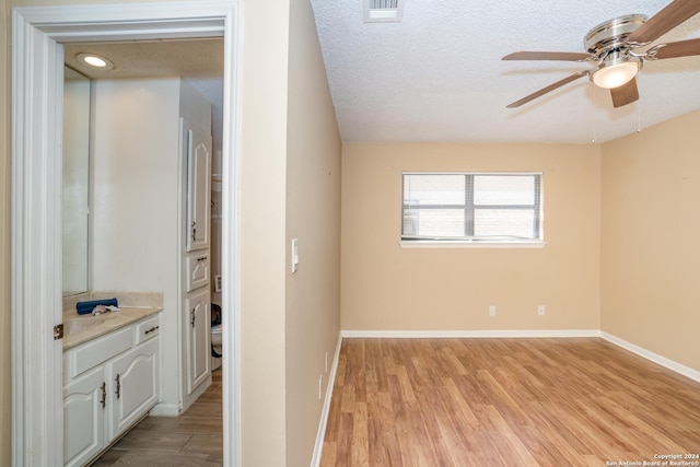 spare room featuring visible vents, a ceiling fan, light wood-style floors, baseboards, and a textured ceiling