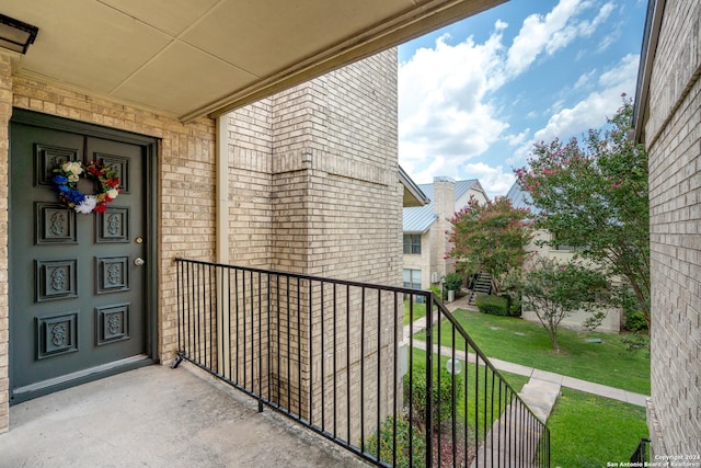 view of exterior entry featuring a lawn, brick siding, and a balcony