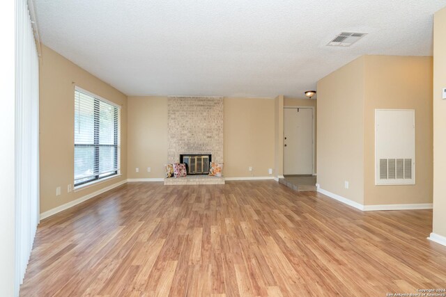 unfurnished living room featuring a textured ceiling, light wood-style floors, a heating unit, a brick fireplace, and visible vents