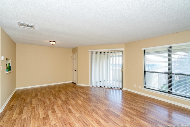 unfurnished room with baseboards, light wood-style flooring, visible vents, and a textured ceiling