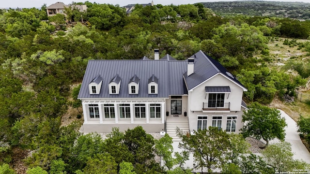 back of house featuring a standing seam roof, a chimney, metal roof, stairway, and stucco siding