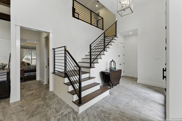 entryway featuring stairs, a chandelier, marble finish floor, baseboards, and a high ceiling