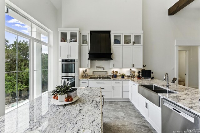 kitchen featuring a high ceiling, a sink, glass insert cabinets, appliances with stainless steel finishes, and custom range hood