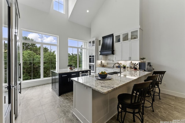 kitchen featuring a towering ceiling, stainless steel appliances, a sink, a kitchen island, and a peninsula