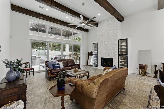 living room with ceiling fan, beamed ceiling, a fireplace, a high ceiling, and visible vents