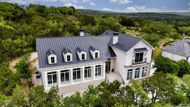 rear view of house with a balcony, a chimney, metal roof, stucco siding, and a standing seam roof