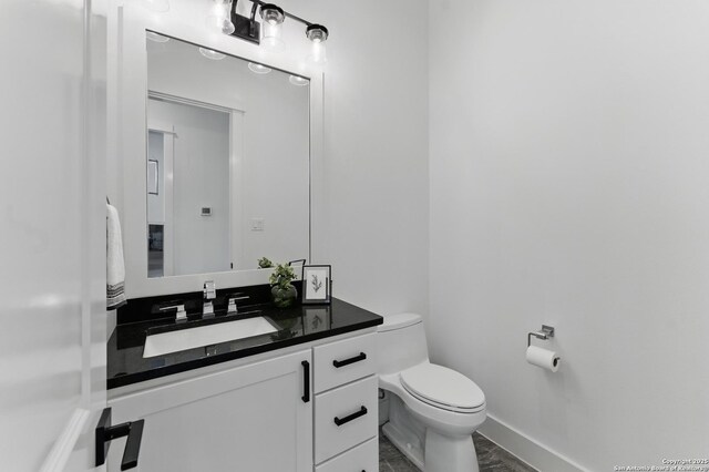 half bath featuring toilet, vanity, and baseboards
