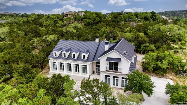 rear view of house featuring a standing seam roof, a chimney, metal roof, a balcony, and stucco siding