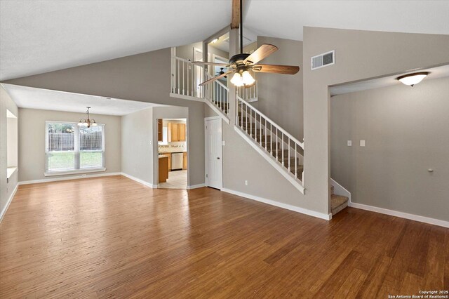 unfurnished living room featuring visible vents, ceiling fan with notable chandelier, wood finished floors, stairway, and high vaulted ceiling