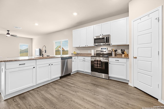 kitchen featuring stainless steel appliances, a ceiling fan, a sink, light wood-style floors, and white cabinetry