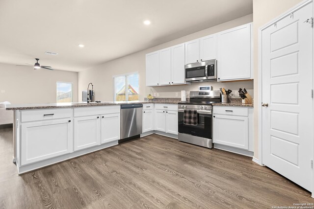 kitchen with stainless steel appliances, white cabinetry, a sink, a peninsula, and dark wood-style flooring