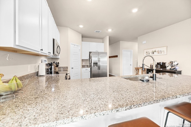 kitchen with white cabinets, stainless steel appliances, visible vents, a sink, and light stone countertops