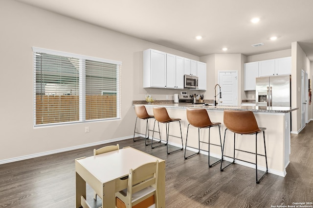 kitchen featuring white cabinets, a sink, a peninsula, appliances with stainless steel finishes, and dark wood-style flooring