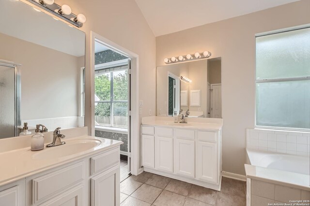 bathroom featuring tile patterned floors, a sink, a bath, lofted ceiling, and two vanities