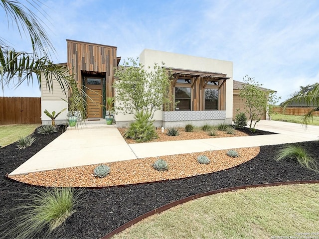 contemporary house with driveway, stucco siding, and fence