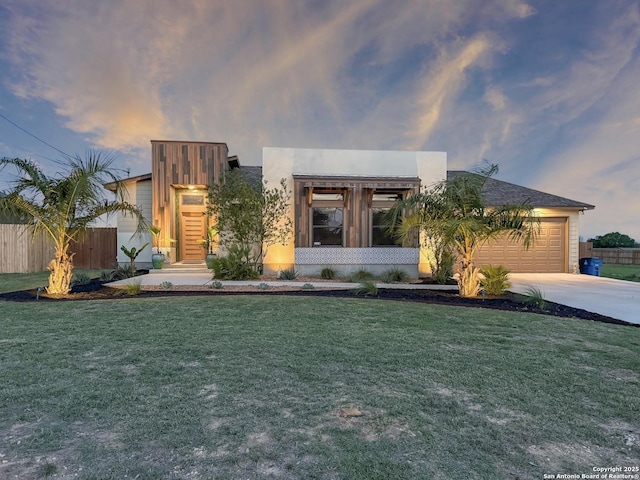 contemporary house with an attached garage, a front lawn, concrete driveway, and fence