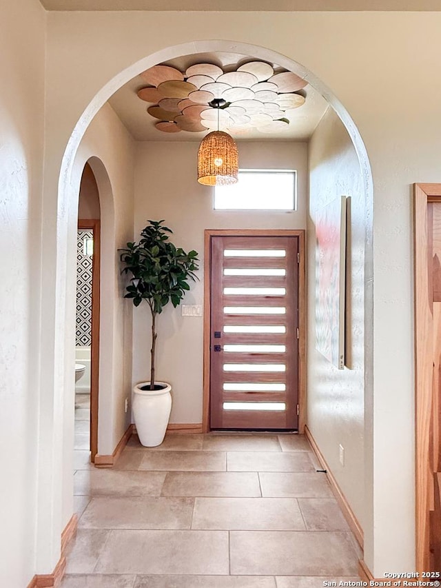 entryway with arched walkways, baseboards, and light tile patterned flooring