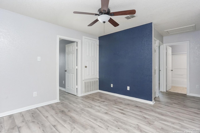 unfurnished bedroom featuring attic access, visible vents, baseboards, wood finished floors, and ceiling fan