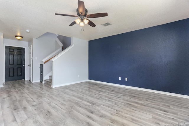 unfurnished living room featuring wood finished floors, visible vents, baseboards, stairs, and ceiling fan
