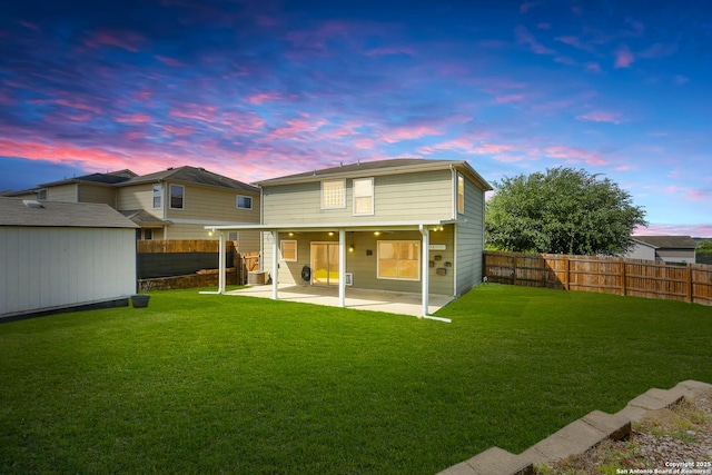 back of house at dusk with a patio, a shed, an outbuilding, a yard, and a fenced backyard