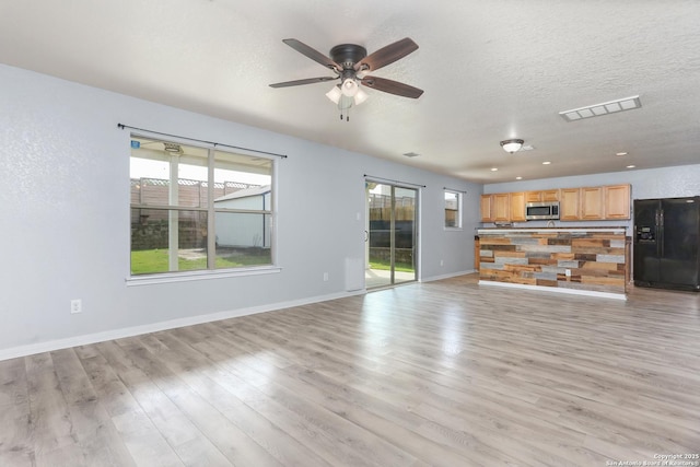 unfurnished living room featuring light wood finished floors, plenty of natural light, a ceiling fan, and visible vents