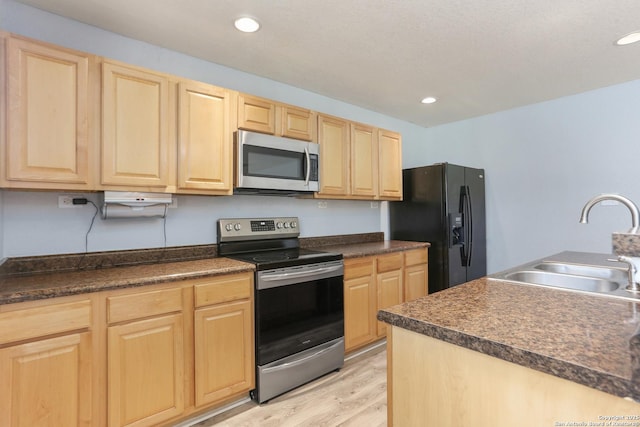 kitchen with dark countertops, light brown cabinetry, a sink, and appliances with stainless steel finishes