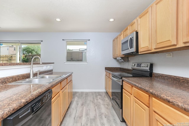 kitchen with light wood finished floors, light brown cabinetry, a sink, dark countertops, and appliances with stainless steel finishes