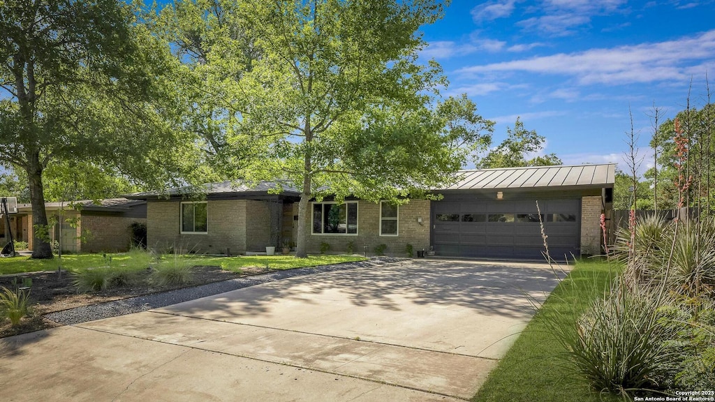ranch-style house with an attached garage, a standing seam roof, driveway, and brick siding