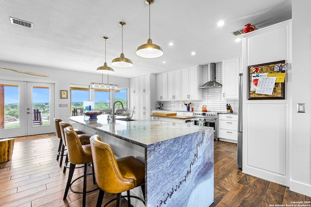kitchen with a sink, high end range, french doors, wall chimney exhaust hood, and visible vents