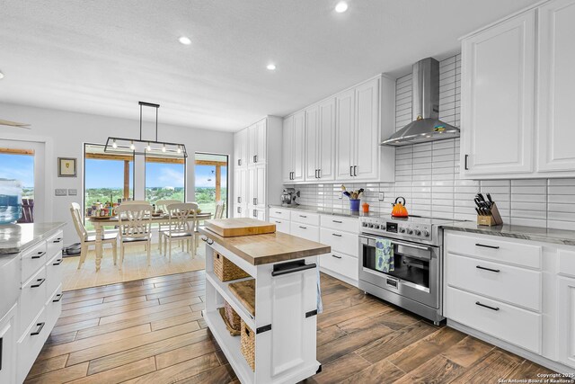 kitchen with high end stainless steel range, butcher block counters, backsplash, wall chimney exhaust hood, and recessed lighting