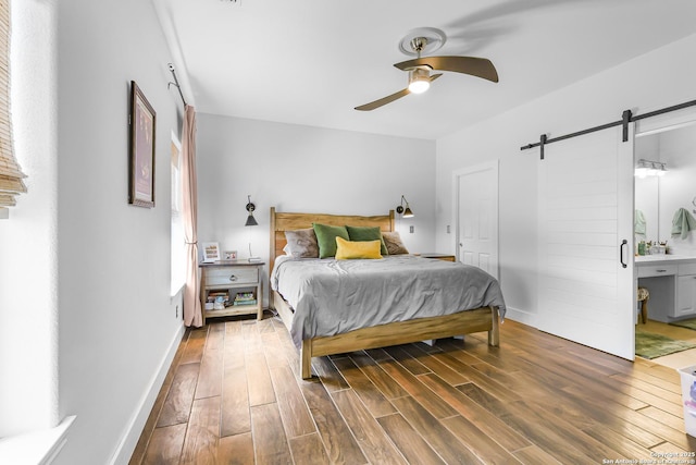 bedroom featuring ceiling fan, wood finished floors, a barn door, and ensuite bathroom